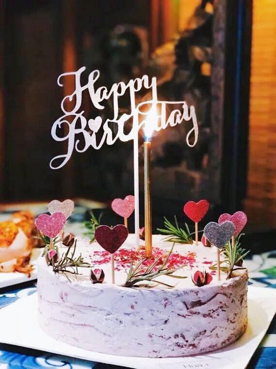 a birthday cake with two candles and hearts on it, sitting on a table in front of other desserts