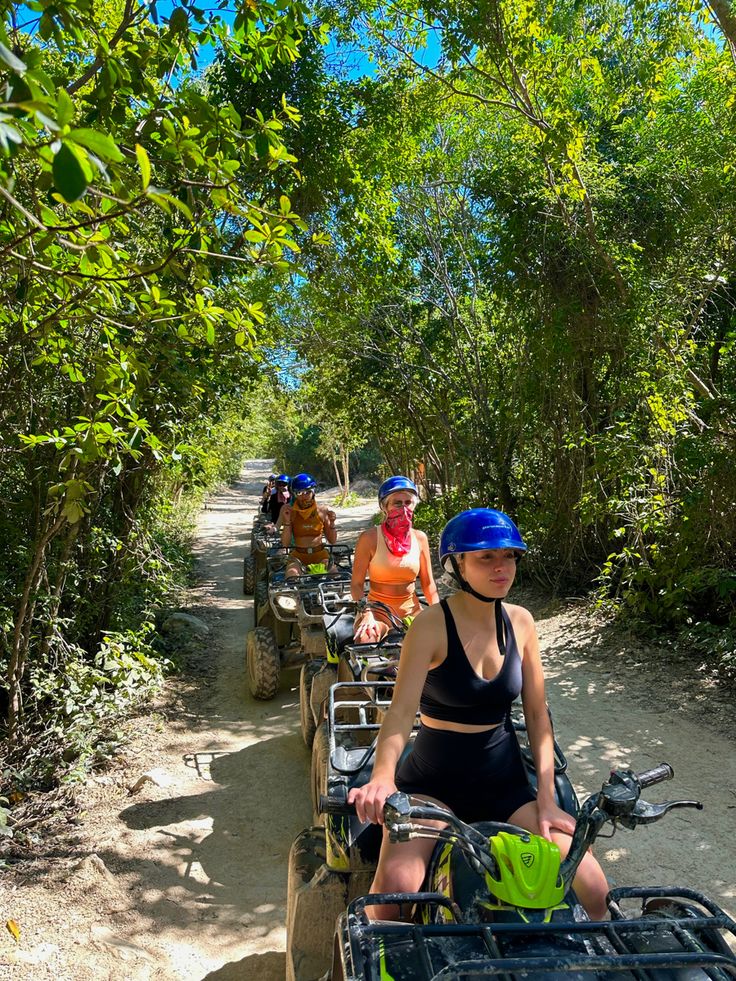 three people riding four wheelers down a dirt road