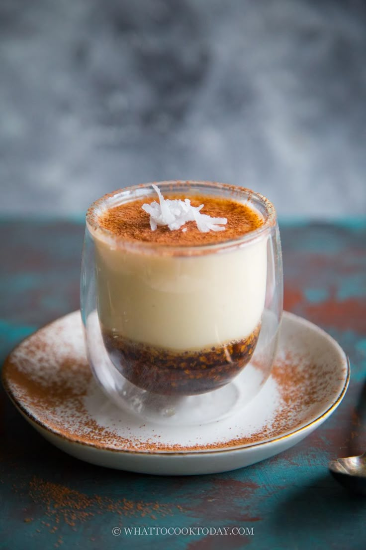 a dessert in a glass on a saucer with spoons next to the plate