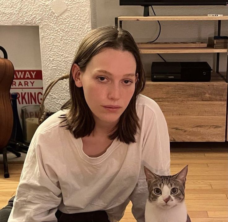 a woman sitting on the floor with a cat in her lap looking at the camera