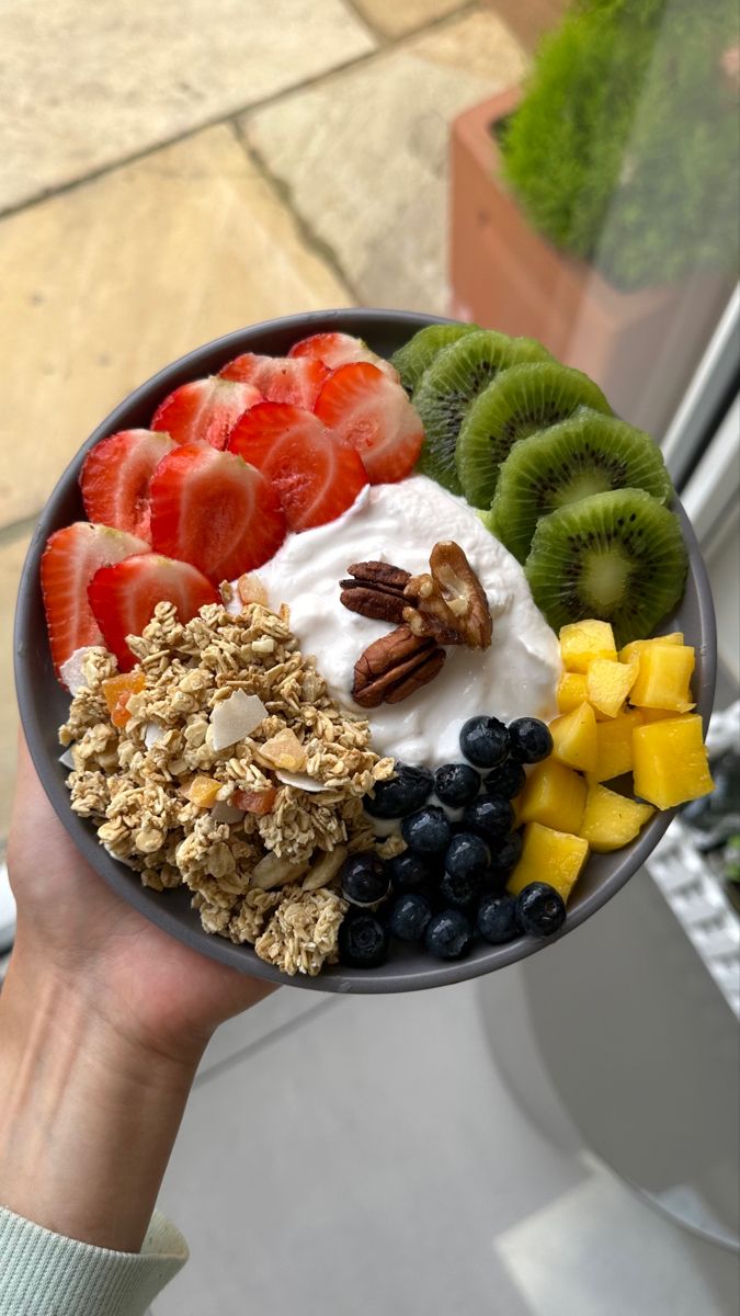 a person holding a bowl filled with fruit and yogurt