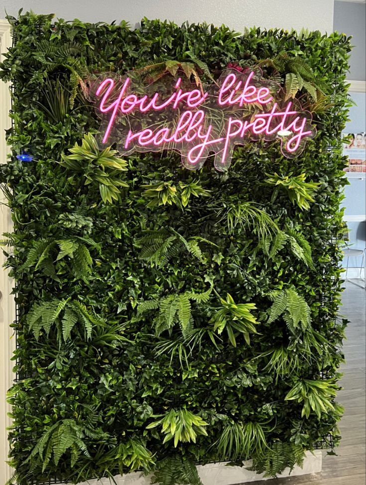 a green wall with plants and neon signs that say you're like really pretty