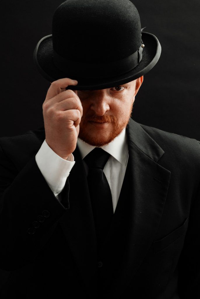 a man in a black suit and top hat is holding his hand to his face