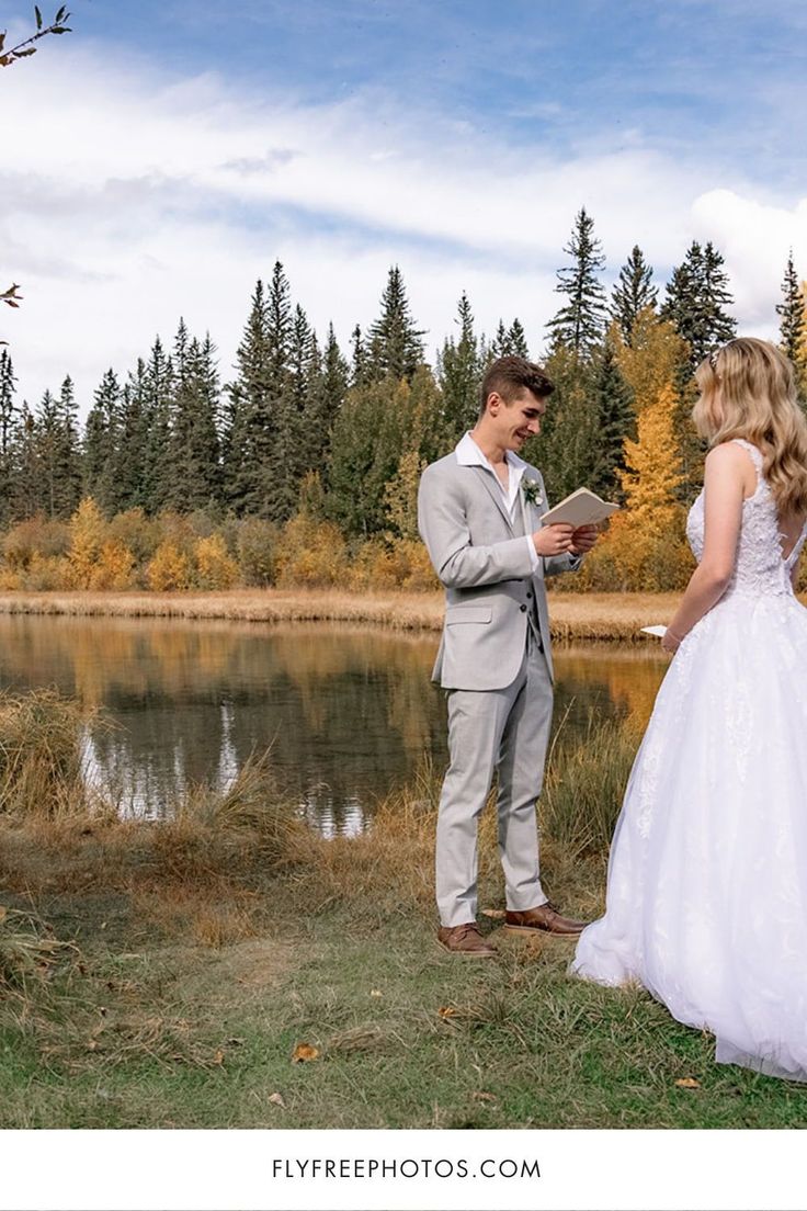 a bride and groom standing in front of a lake