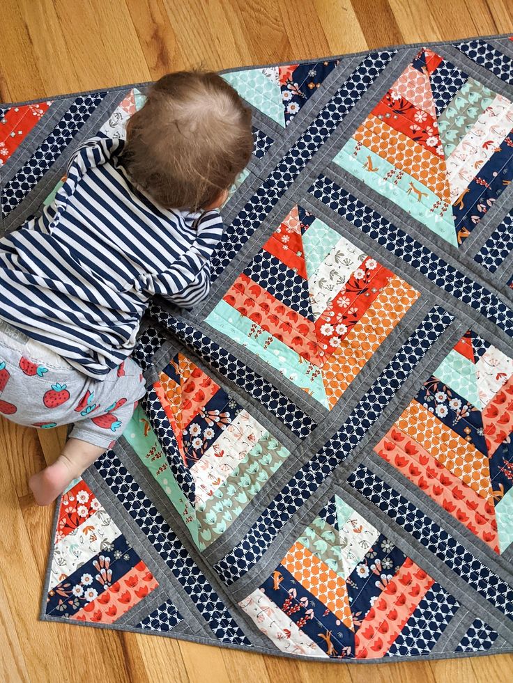 a baby is playing with a quilt on the floor