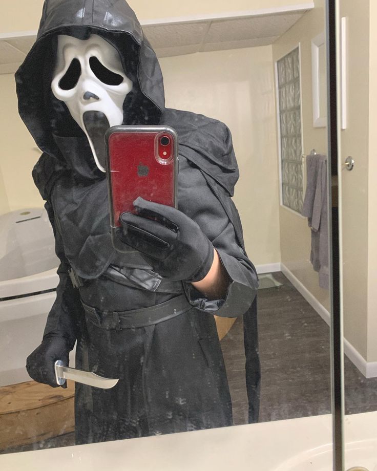 a person in a ghost costume holding a cell phone and taking a selfie with the mirror behind them