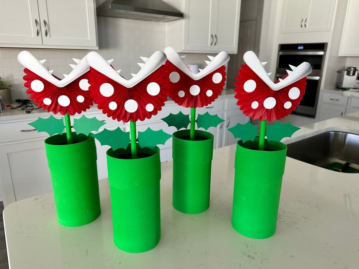 three green vases with red and white flowers in them sitting on a kitchen counter