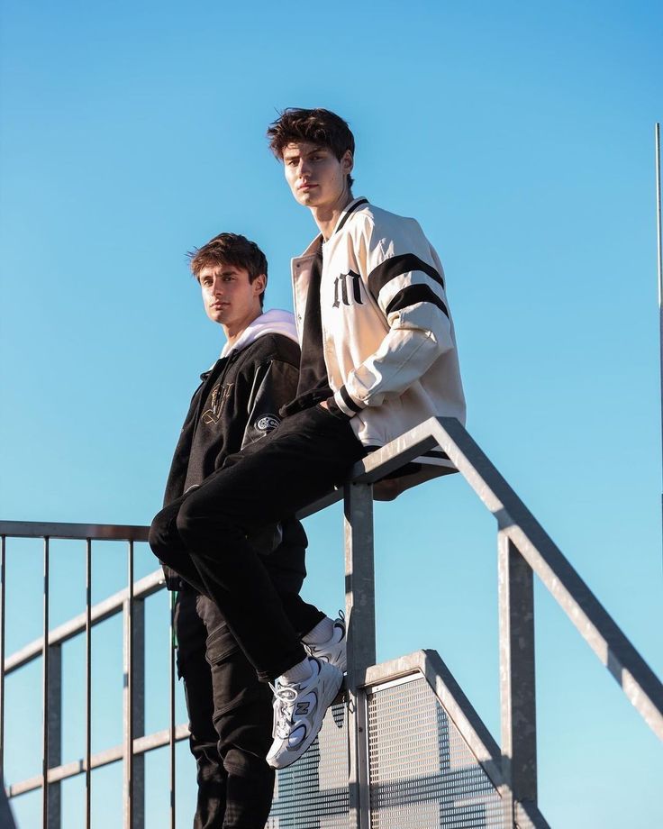 two young men standing on top of a metal hand rail next to each other in front of a blue sky