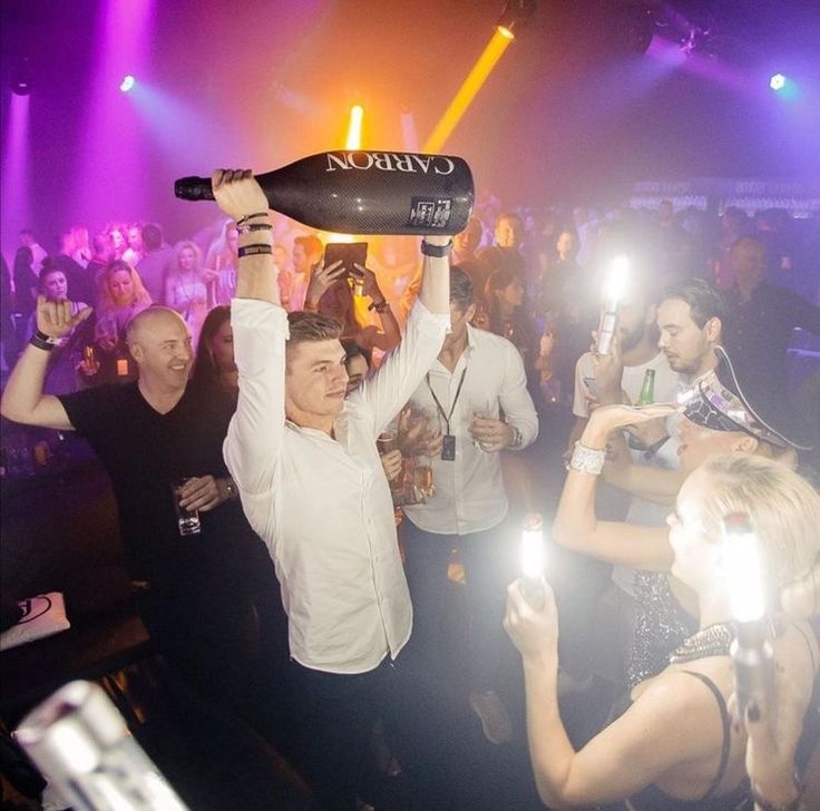 a man is holding up a bottle in the air at a party with other people