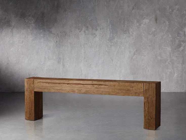 a wooden bench sitting on top of a cement floor in front of a concrete wall