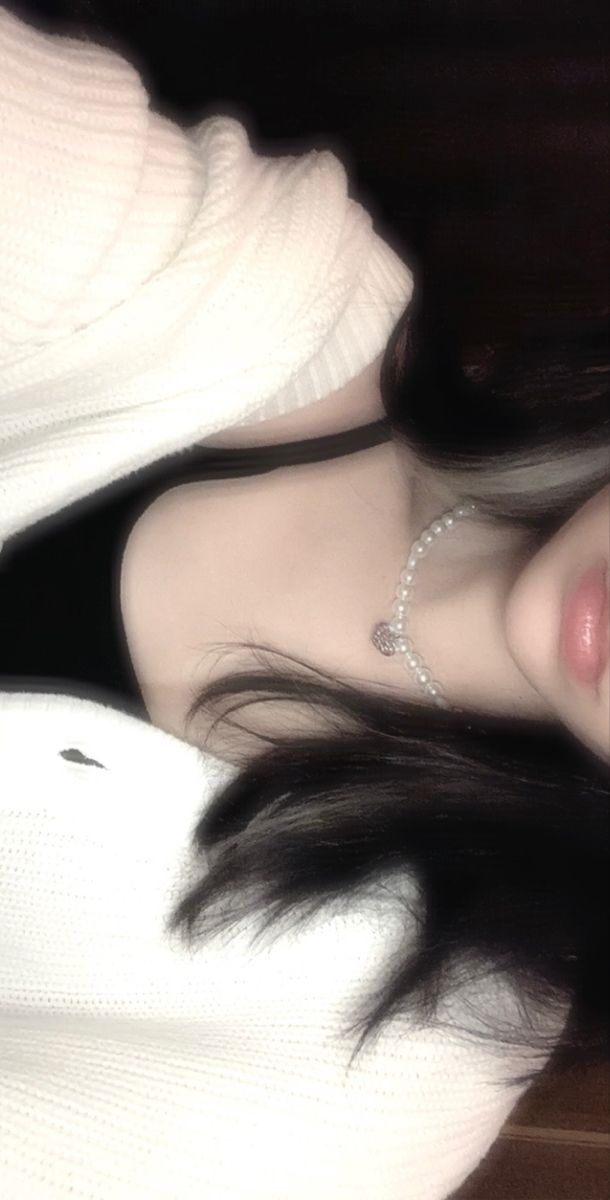 a woman with long black hair wearing a white sweater and diamond necklace on her neck