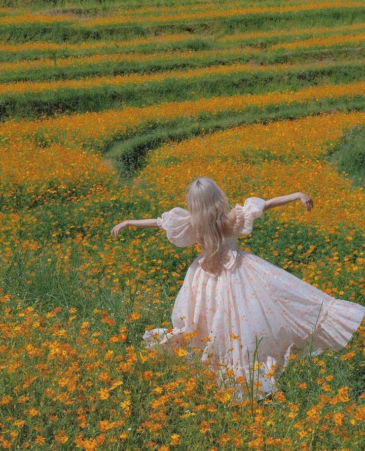 a woman in a white dress standing in a field full of yellow and orange flowers