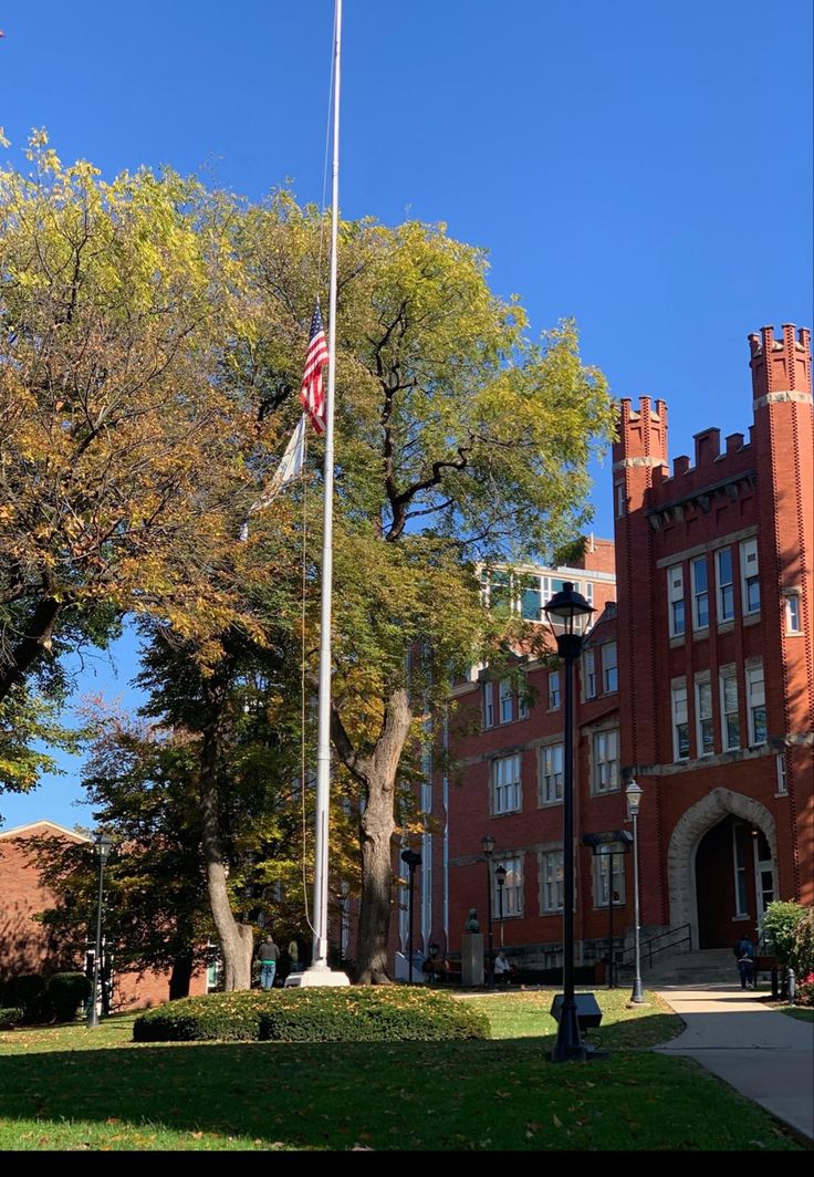 an american flag is flying in front of a brick building with trees and grass on the lawn