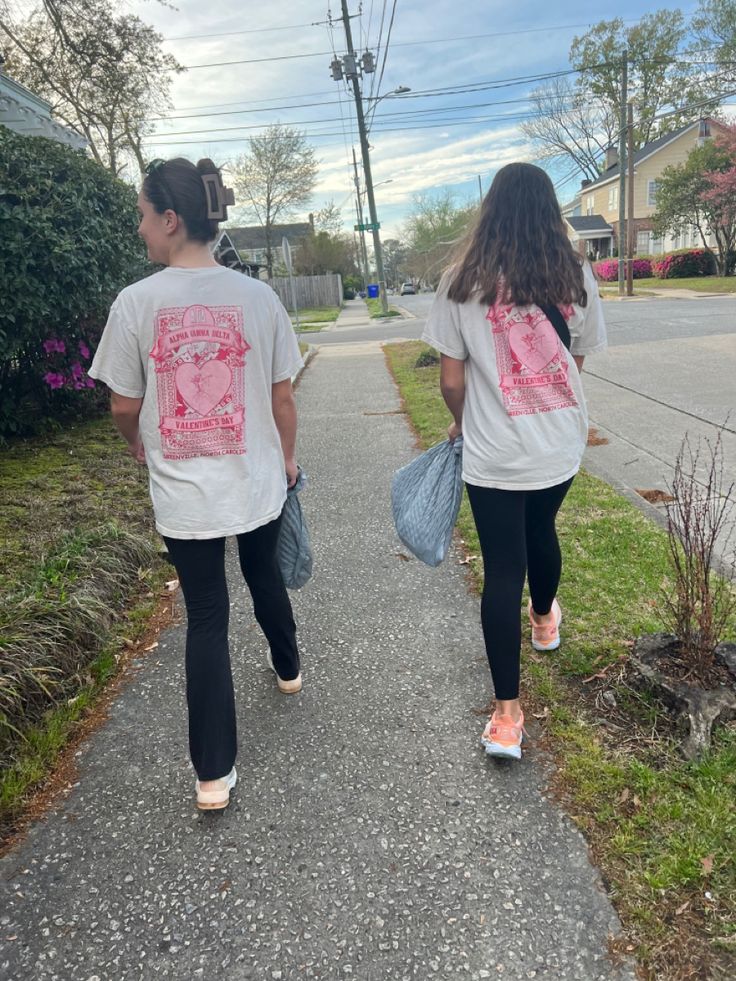 two girls are walking down the sidewalk with their back to the camera and holding bags