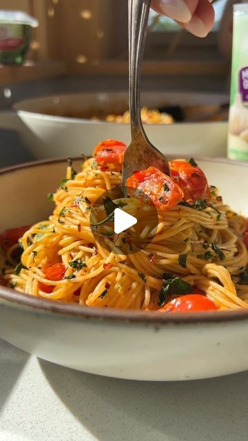 someone is eating spaghetti with tomatoes and spinach in a bowl next to a carton of yogurt