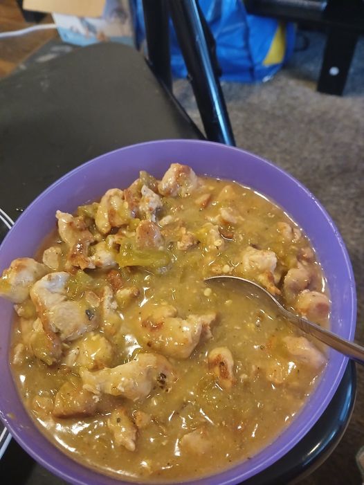 a purple bowl filled with food on top of a table next to a metal spoon