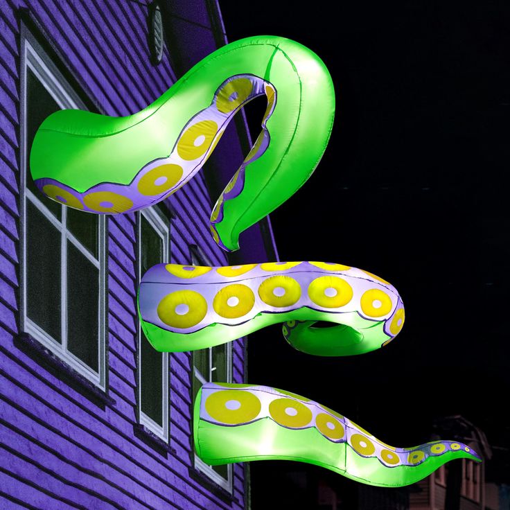 two large green and yellow bananas hanging from the side of a purple building at night