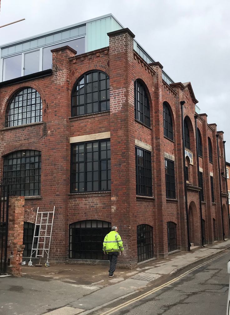 a man standing in front of a tall brick building with windows on the top floor