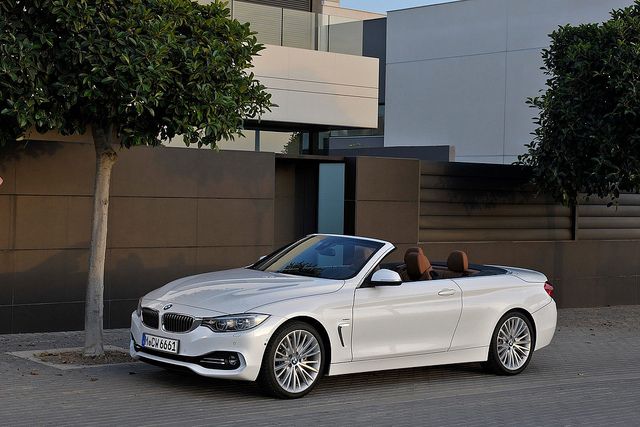 a white convertible car parked in front of a building next to a tree and bushes