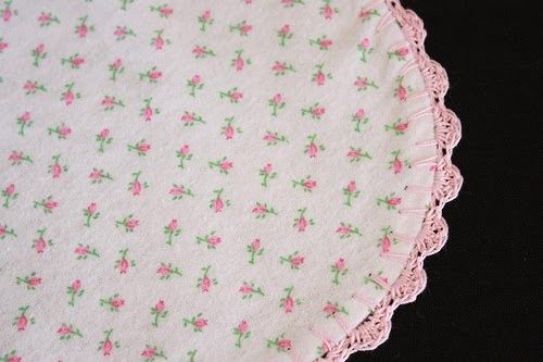 a pink and green flowered doily on a black tablecloth with white crochet