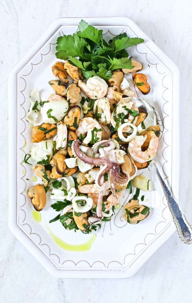 a white plate topped with shrimp, onions and green garnish next to a fork