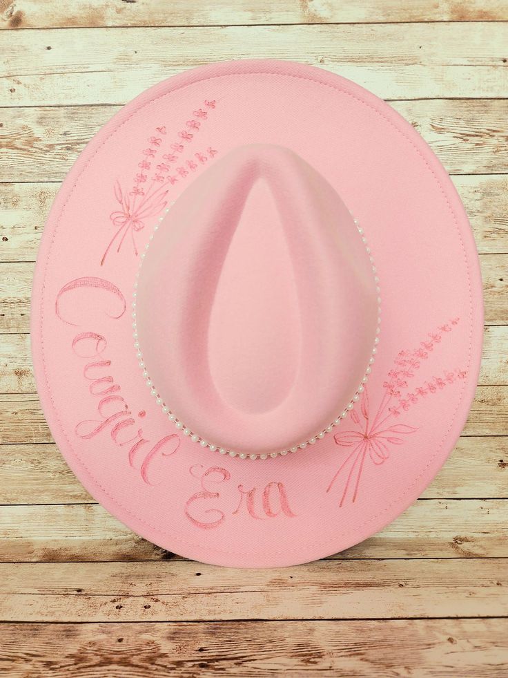 Ladies burned felt hat. All hats are hand-burned by the artist so they are all unique. Each hat is complimented with a band and accessories to accentuate the design. This hats is a sweet baby pink with lace and pearls.  "Cowgirl Era" is hand written by the artist and is complimented by hand burned wild flowers. Pink Burned Hat, Custom Felt Hat For Country Events, Custom Flat Brim Felt Hat For Western-themed Events, Custom Felt Hat For Rodeo, One Size, Custom Handmade Top Hat For Country Events, Custom Adjustable Felt Hat For Western-themed Events, Adjustable Brimmed Mini Hats In Felt, Handmade Country Style Top Hat For Country Events, Adjustable Felt Fedora Mini Hat