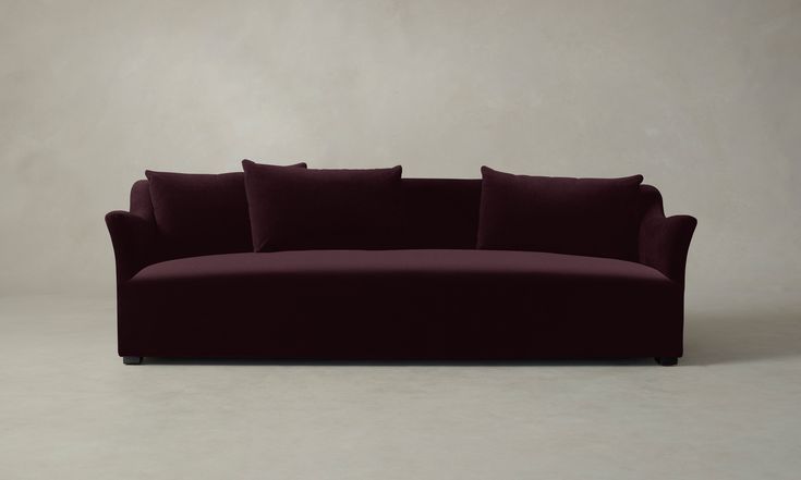 a red couch with pillows on it in front of a white wall and grey floor