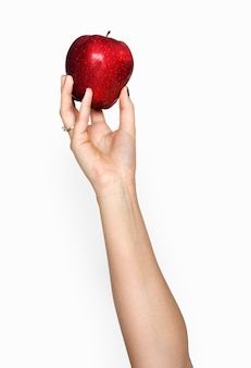 a woman's hand holding an apple up to the camera, against a white background