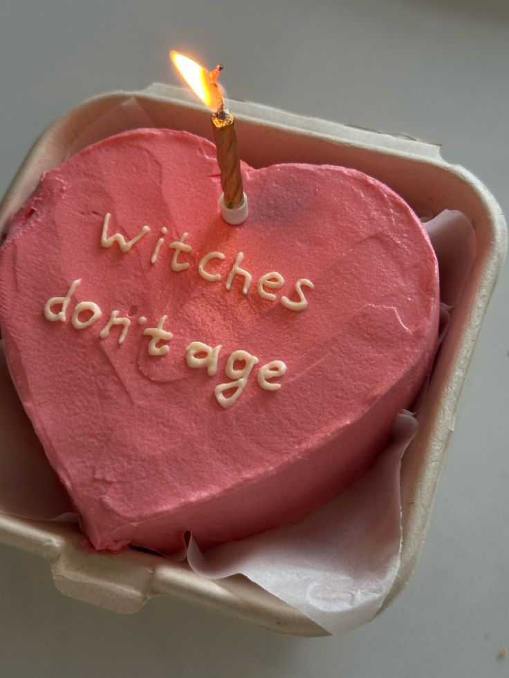 a pink heart shaped cake with a lit candle in it that says witches don't age