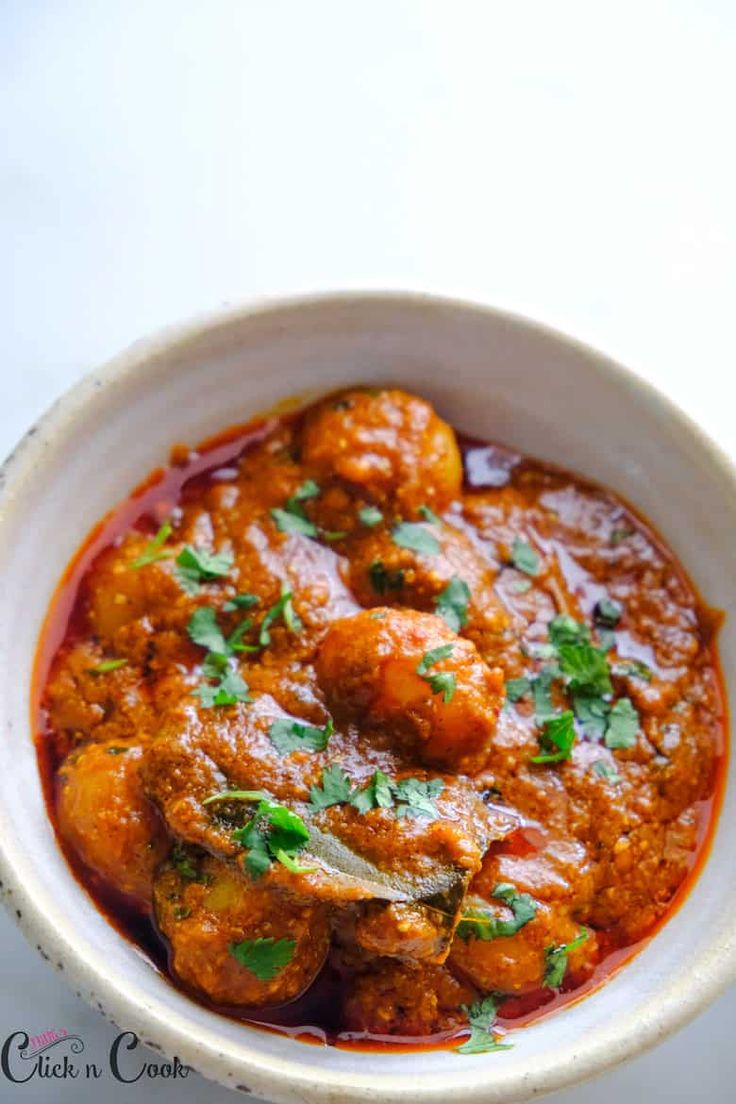 a white bowl filled with meatballs and garnished with cilantro leaves