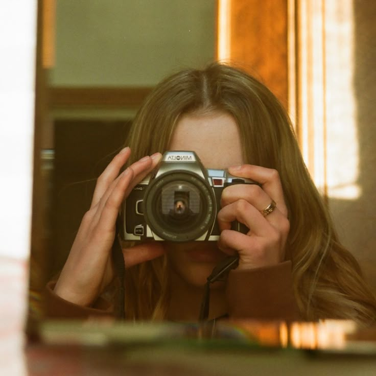 a woman taking a selfie in front of a mirror holding a camera up to her face