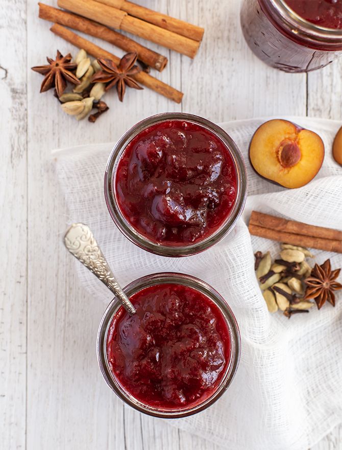 two jars filled with jam sitting on top of a white table next to cinnamons and apples