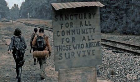 three people walking down the railroad tracks with backpacks on their backs and an old sign reading sanctuary for all community for all those who arrive