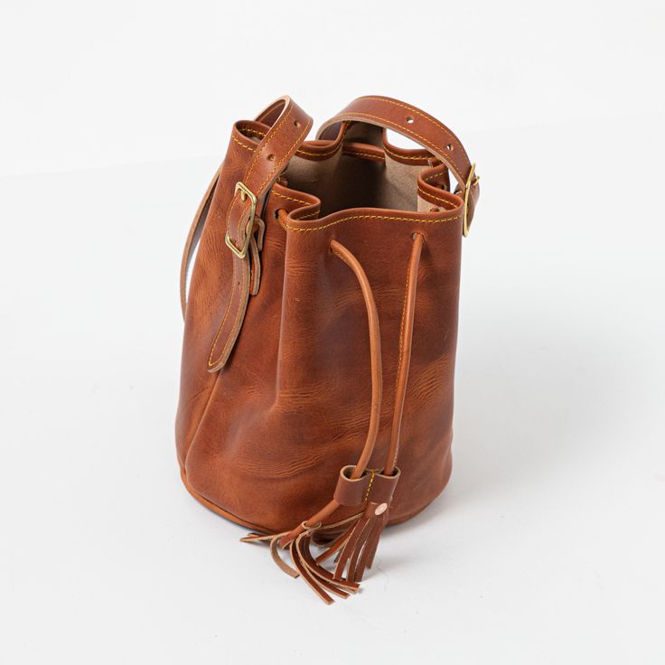 The English Tan Dublin Bucket Bag is an heirloom-quality bag handmade of full-grain leather. English Tan Dublin is a thick, waxed leather with a smooth grain and dramatic pull-up, produced by the Horween tannery in Chicago. Leather Bucket Satchel As A Gift, Cognac Smooth Grain Bucket Bag, Cognac Smooth Grain Satchel Bucket Bag, Classic Leather Satchel Bucket Bag, Leather Bucket Bag With Leather Lining, Cognac Leather Bucket Bag With Smooth Grain, Classic Leather Bucket Bag In Cognac, Leather Shoulder Bucket Bag With Smooth Grain, Leather Bucket Bag With Smooth Grain As Shoulder Bag