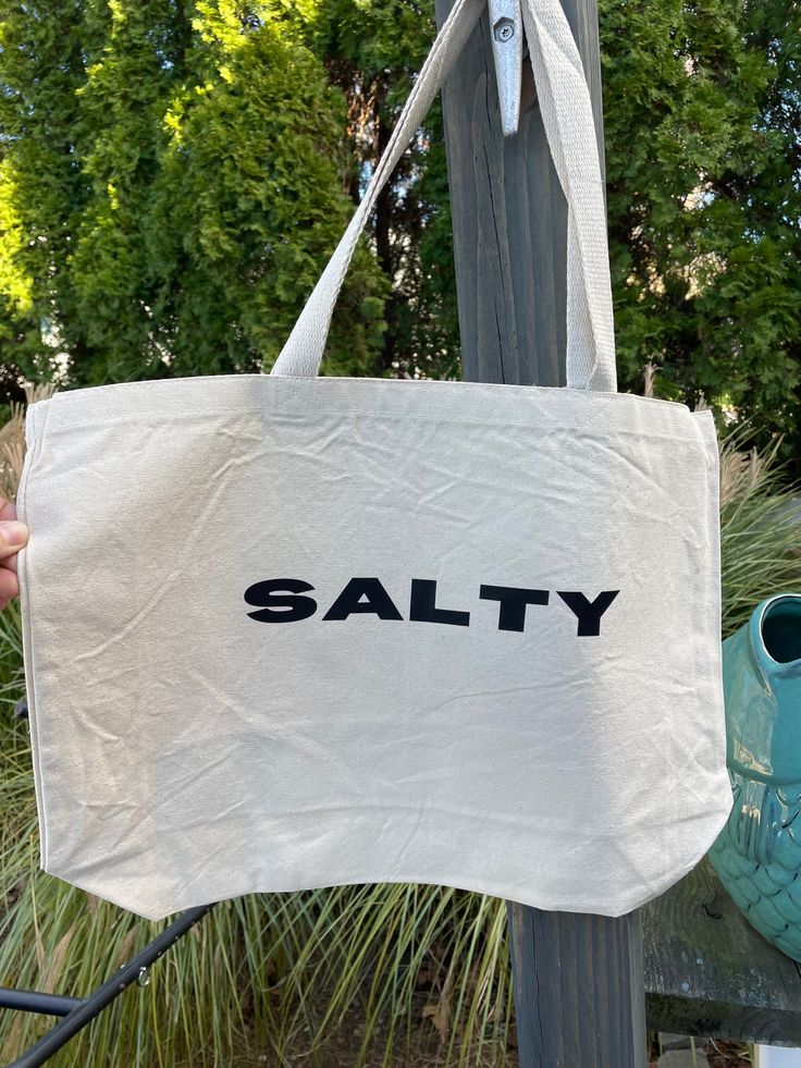 Stay salty no matter the season with the Salty Tote Bag! This extra large bag is perfect for carrying all the essentials — and then some. Bring it to the beach, farmer's market, campus, or run errands. This one can do it all and bring you beach style no matter where you go. Measures 20"W x 15"H x 5"D Casual Cotton Beach Bag For Travel, Casual Canvas Beach Bag For Daily Use, Cotton Shoulder Bag For Everyday Beach Use, Everyday Cotton Shoulder Bag For Beach, Large Capacity Cotton Bag For Beach Season, Large Capacity Casual Canvas Beach Bag, Casual Canvas Bag For Everyday Beach Season, Casual Large Capacity Canvas Beach Bag, Casual Large Capacity Canvas Bag For Beach Season