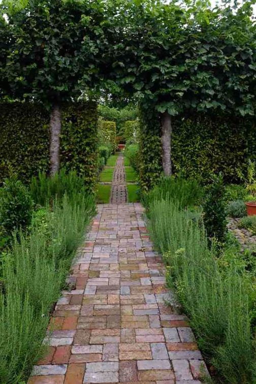 a brick pathway between two trees in a garden with lots of greenery on either side