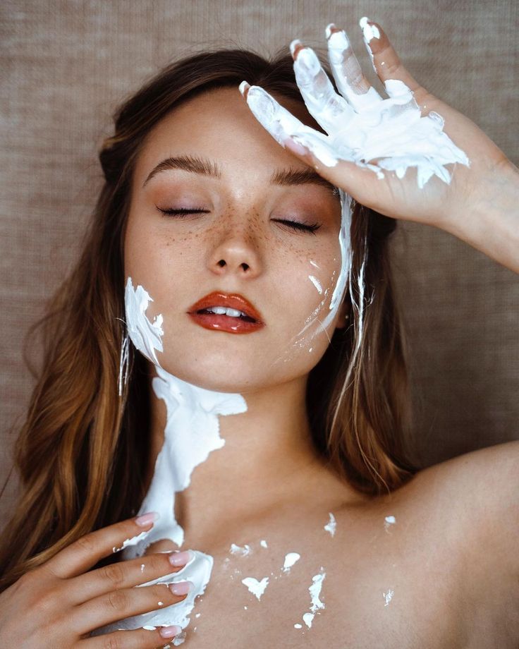 a woman with white paint on her face and hands over her head, covering her eyes