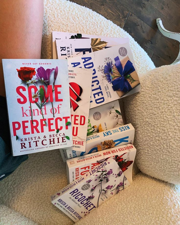 a pile of books sitting on top of a white chair next to a person's leg