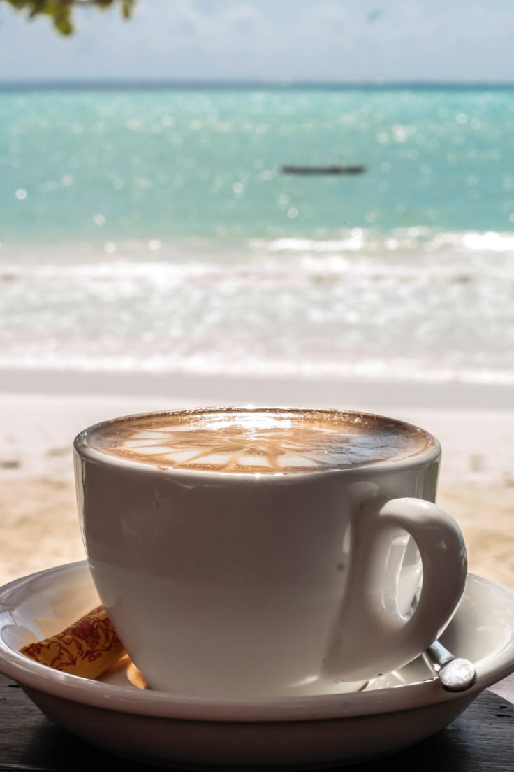 a cup of coffee sitting on top of a white saucer next to the ocean