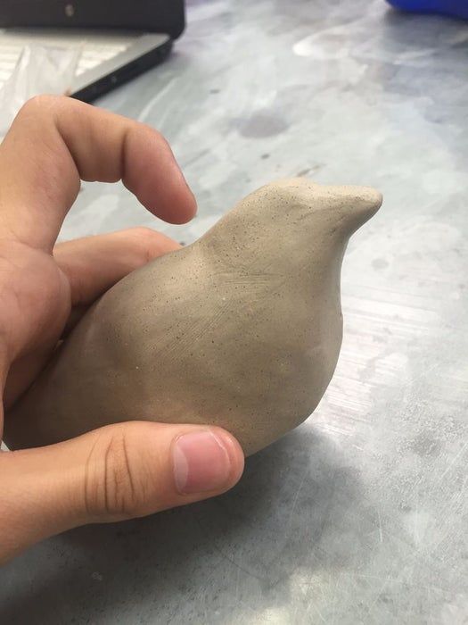 a hand holding a clay bird on top of a table