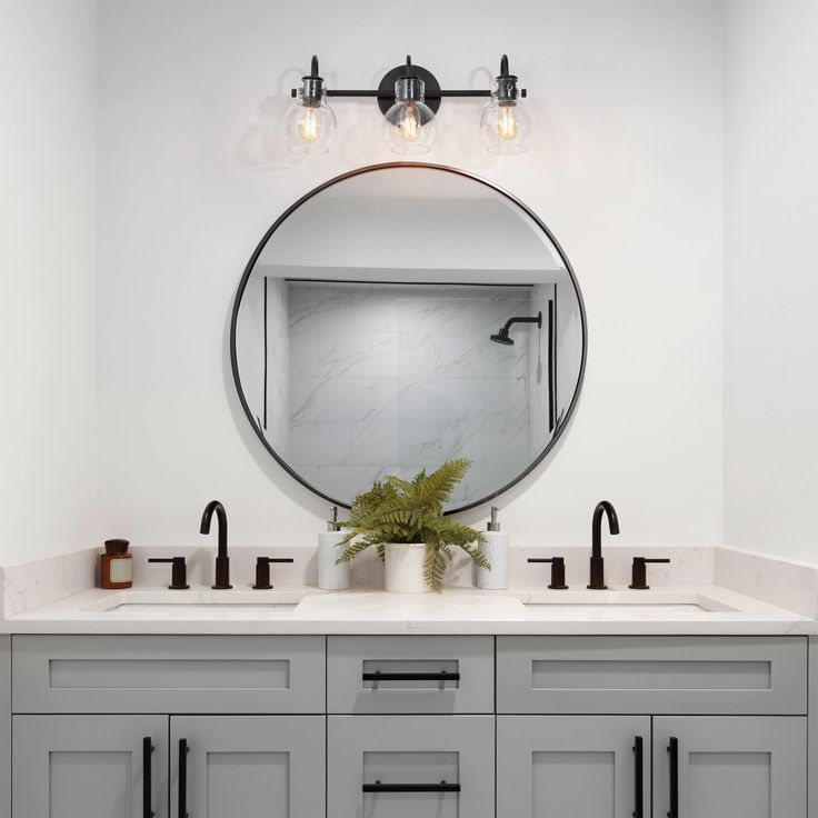 a bathroom with two sinks and a large round mirror above the sink is surrounded by gray cabinetry