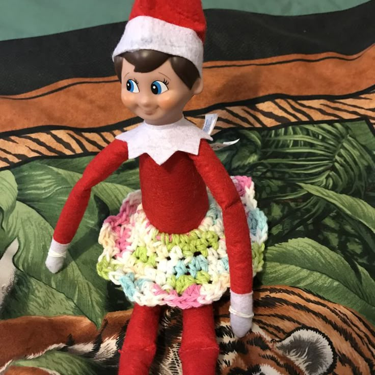 an elf is sitting on top of a bed with a crocheted skirt and hat