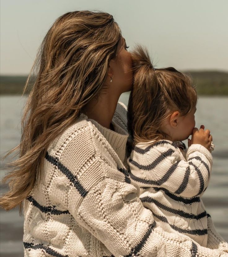 a woman holding a small child in her arms by the water's edge,