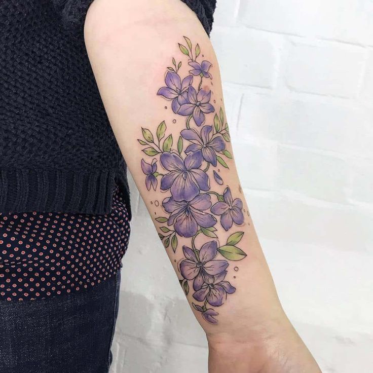 a woman's arm with purple flowers and leaves on the left side of her arm