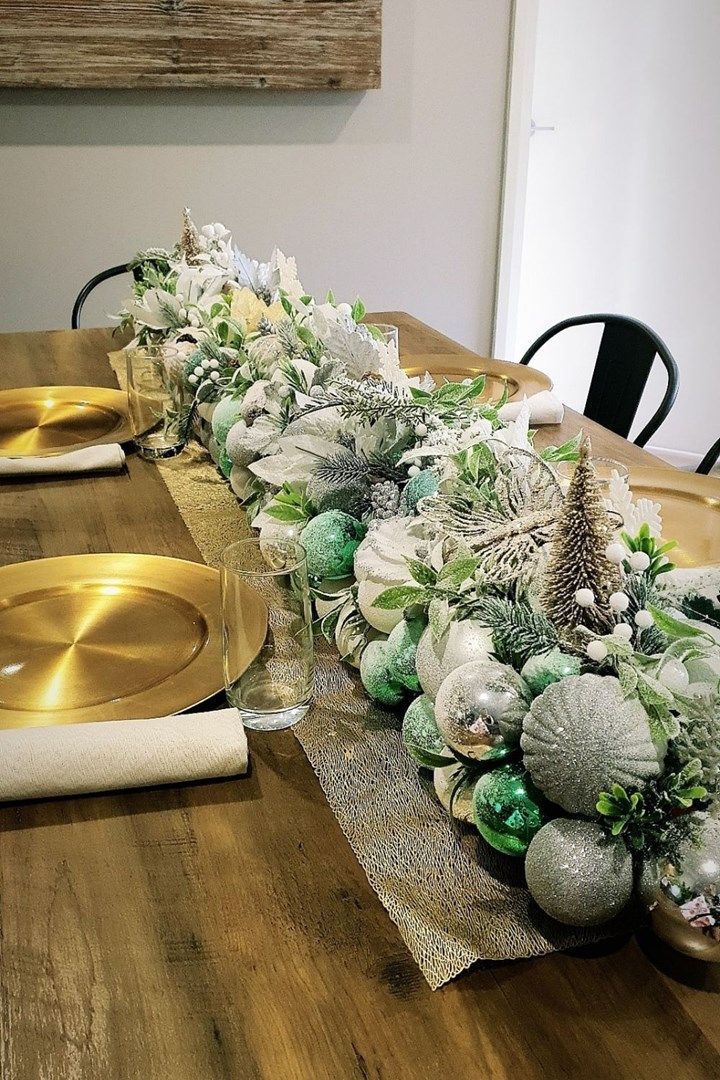 the table is set with silver and green christmas decorations on it, along with gold plates