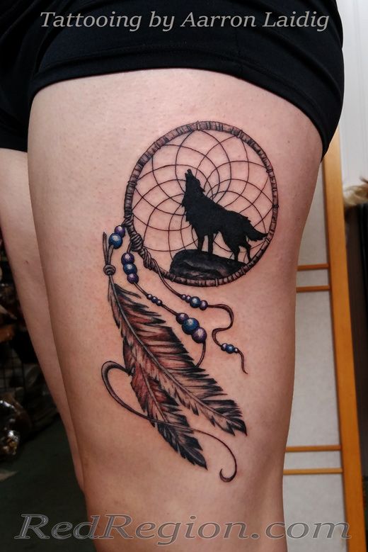 a woman's thigh with a wolf and dream catcher tattoo on it