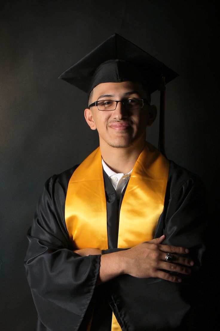 a man in a graduation cap and gown with his arms crossed posing for the camera