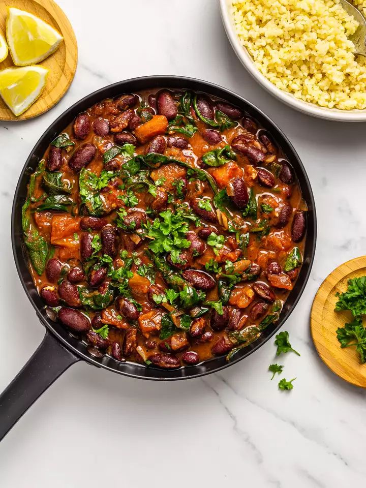 a skillet filled with beans and greens on top of a counter next to rice