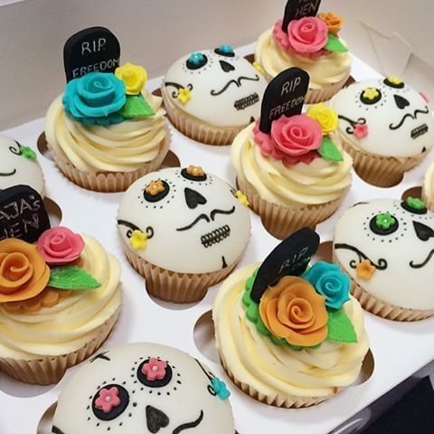 cupcakes decorated with sugar skulls and flowers are displayed in a box on a table