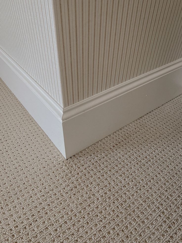 the corner of a room with carpeting on the floor and white trim around it